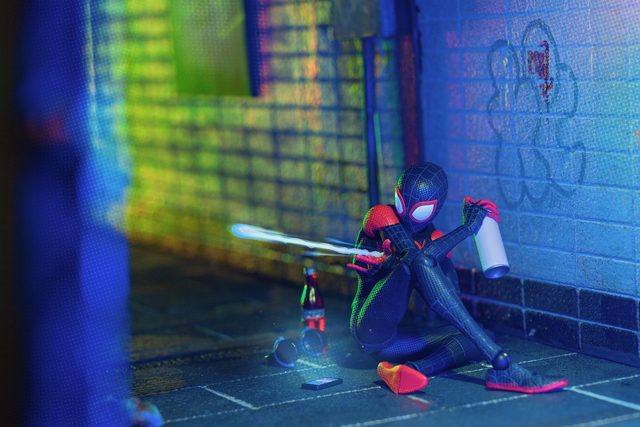 Une figurine de Spider-Man assise contre un mur carrelé, en train de le taguer sous une lumière néon