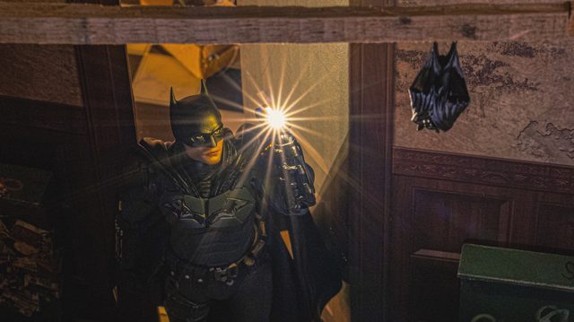 Une figurine de Batman dans une pièce sombre en bois, une lumière vive jaillissant de sa main levée