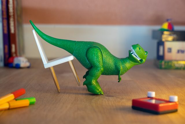 Rex, le dinosaure vert en jouet, tirant une petite chaise blanche sur un bureau