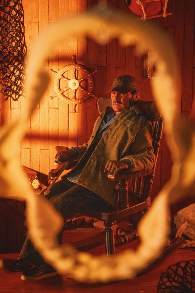 Une figurine de pêcheur dans un rocking-chair, vue à travers une mâchoire de requin, dans une cabine aux tons orangés