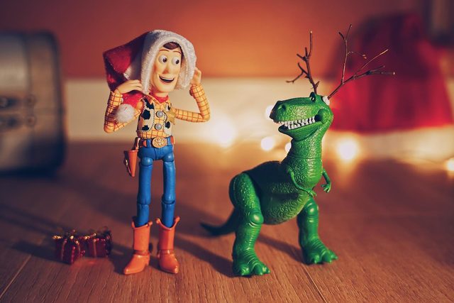 Woody in a Santa hat next to Rex wearing twig antlers, with warm fairy lights behind them