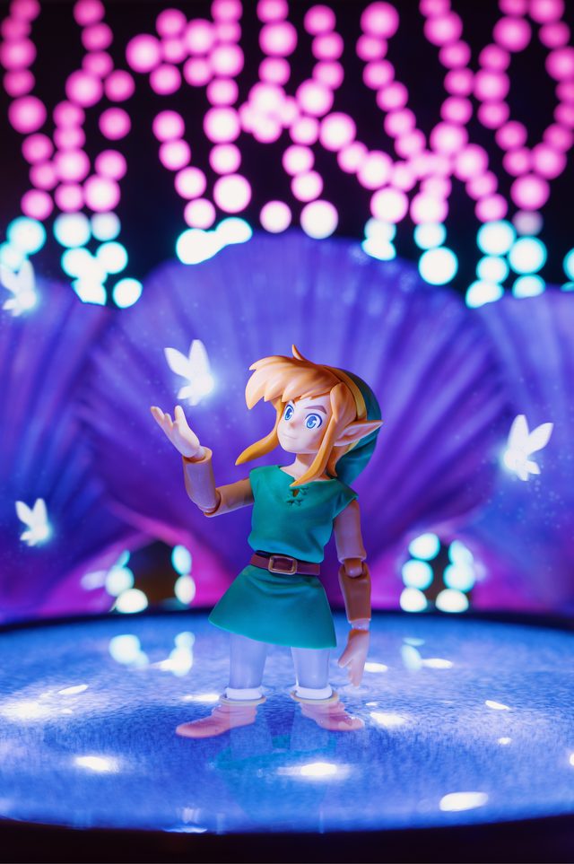 A Link figure reaching for glowing fairies on a blue-lit fountain, with pink bokeh above