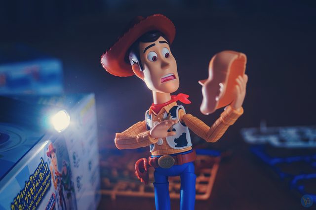 Woody looking horrified at a face he is holding in his hand, lit by a small lamp